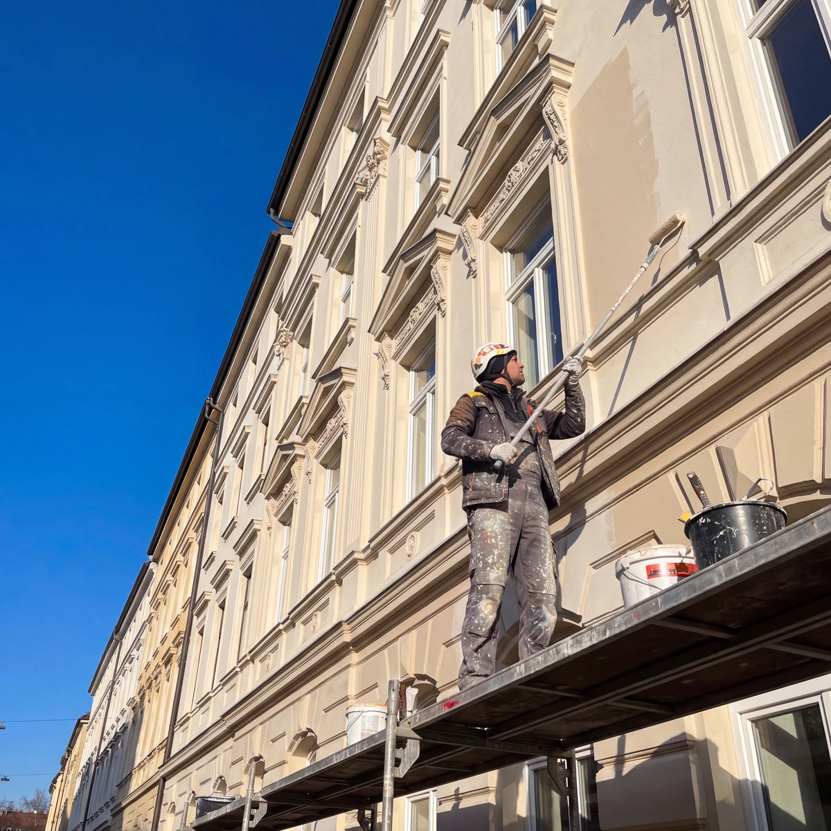 Maler auf dem Gerüst beim Fassadenanstrich im Rahmen der Fassadensanierung in München
